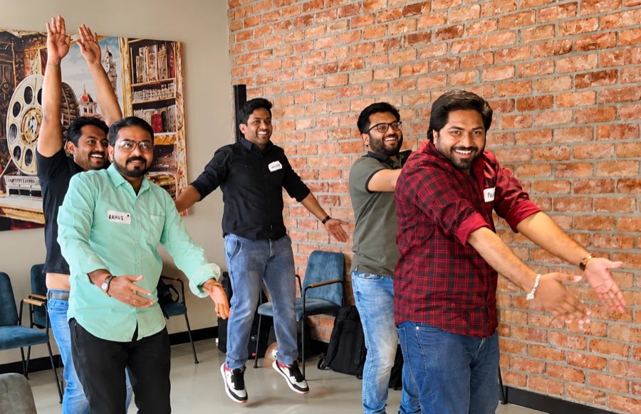 Five first-time managers on their feet mid-exercise, mirroring a movement and laughing