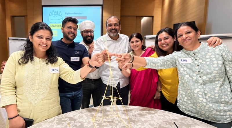 Managers gathered around the spaghetti-and-marshmallow tower they have just built