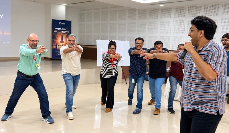 A row of managers copying a movement led by a Change+ facilitator holding a microphone